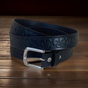 May include: A black leather belt with a silver buckle. The belt is embossed with a repeating pattern of skulls.