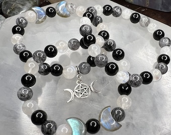 May include: Three beaded bracelets with a celestial theme. The bracelets feature a mix of black, white, and gray beads, along with crescent moon and star charms. The beads are arranged in a circular pattern.
