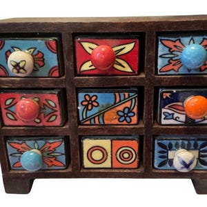 May include: A dark brown wooden storage chest featuring nine individual drawers. Each drawer front is decorated with colorful, hand-painted ceramic patterns in shades of red, blue, orange, and yellow, and includes a small, round ceramic knob.