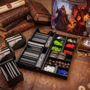 Può includere: Un organizer nero per giochi da tavolo contenente mazzi di carte, gettoni in plastica colorati e dadi. Il set include tre portacarte separati e un vassoio principale con scomparti, esposto accanto a una scatola di gioco, libri e un calice.