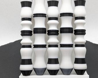 Puede incluir: Cinco objetos decorativos blancos, negros y grises con un diseño similar al bambú. Cada objeto tiene una base blanca, una banda negra, un centro blanco, otra banda negra y una parte superior gris. Están dispuestos verticalmente sobre una base rectangular blanca.