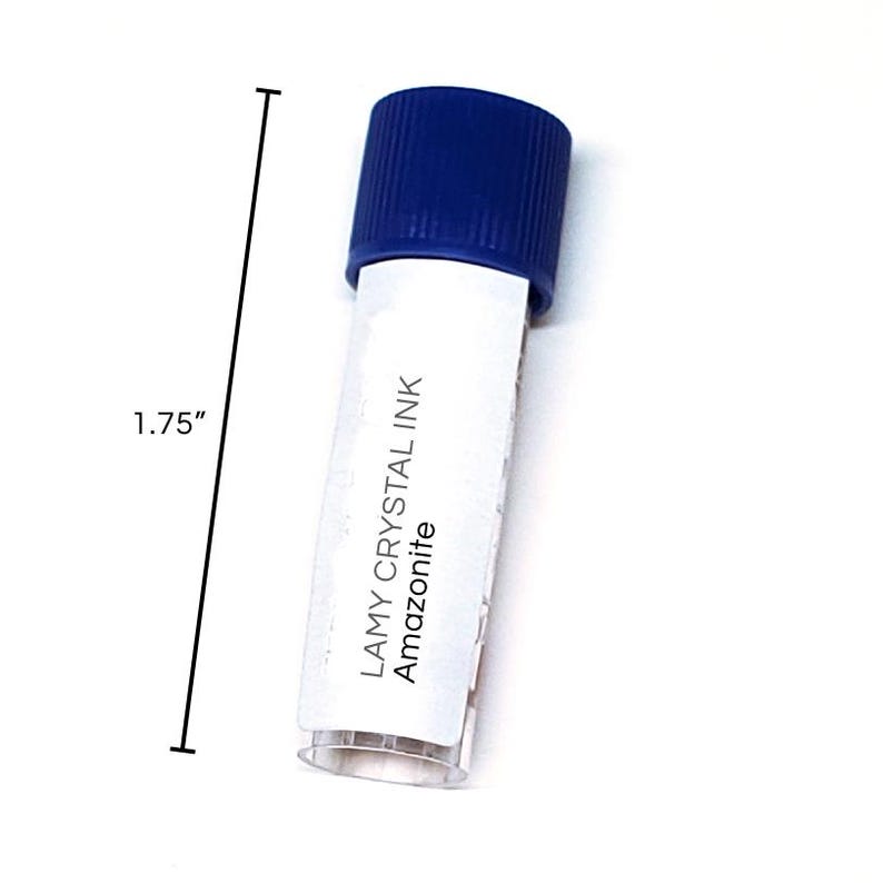 May include: A small, clear tube of Lamy Crystal Ink in Amazonite. The tube is capped with a dark blue lid. The tube is approximately 1.75 inches in length. The text "LAMY CRYSTAL INK Amazonite" is printed on the tube.