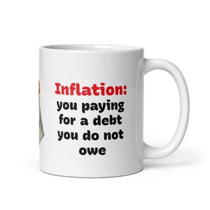 Può includere: Tazza in ceramica bianca con manico curvo. La tazza presenta il testo "Inflation: you paying for a debt you do not owe" in lettere nere e rosse. Un grafico di banconota da un dollaro è parzialmente visibile.