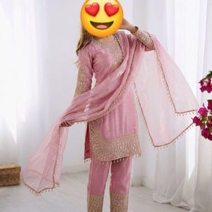 Puede incluir: Conjunto salwar kameez rosa claro bordado. El atuendo incluye una túnica de manga larga, pantalones a juego y un dupatta transparente. El bordado dorado acentúa el escote, las mangas y los puños del pantalón. El dupatta tiene un ribete de cuentas.