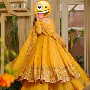 May include: A vibrant yellow formal dress with intricate embroidery and mirror work along the hemline and sleeves. The dress features a flowing silhouette with a matching dupatta. The design includes floral and geometric patterns.