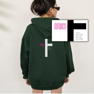 May include: A dark green hooded sweatshirt with a white cross and the text "LGBTQIA2S+" and "YOU NEVER WALK ALONE" in pink lettering.