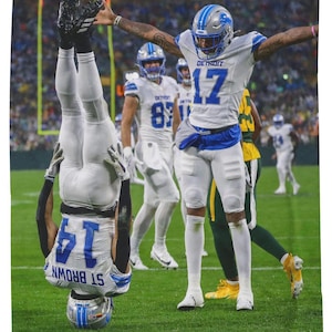 May include: A football player wearing a white and blue uniform with the number 17 on it, celebrates a touchdown while another player wearing a white and blue uniform with the number 14 on it, is upside down in the air.
