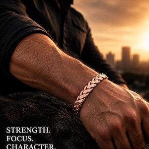 May include: A metallic copper-coloured bracelet featuring a braided link design. The text STRENGTH. FOCUS. CHARACTER. PURE COPPER. PURE CONFIDENCE. is visible in the lower left corner of the image, presented in a clean, sans-serif white font.