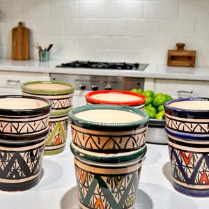Peut inclure: Ensemble de tasses en céramique colorées avec des motifs géométriques. Les tasses présentent des couleurs variées, dont le noir, le vert, le bleu et le rouge, avec des intérieurs crème. Disposition sur un comptoir blanc dans une cuisine.