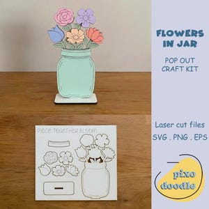 Puede incluir: Un kit de manualidades de madera con un tarro verde menta con flores de colores. Las flores incluyen rosas rosas, flores moradas y melocotón y tulipanes azules. El texto "FLOWERS IN JAR" y "POP OUT CRAFT KIT" son visibles.