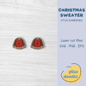 Könnte beinhalten: Zwei Holz-Ohrstecker mit Weihnachtspullover-Motiv. Jeder Ohrring ist eine Miniaturreplik eines festlichen Pullovers mit rotem Körper und grünen und weißen Akzenten. Die Ohrringe sind lasergeschnitten.