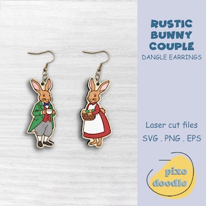 May include: Wooden dangle earrings featuring a rustic bunny couple design. One bunny wears a green coat and holds a teacup, the other wears a red dress and carries a basket of eggs. The text reads "RUSTIC BUNNY COUPLE DANGLE EARRINGS".