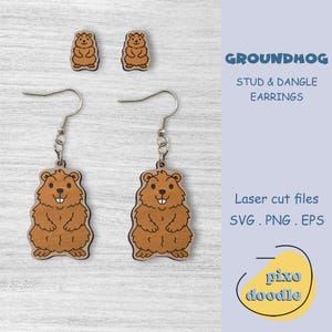Puede incluir: Un par de pendientes colgantes de madera con un diseño de marmota de dibujos animados. Los pendientes son marrones con un contorno marrón claro. La marmota está de pie con las patas delante de ella. Los pendientes están etiquetados como "Groundhog Stud & Dangle Earrings".