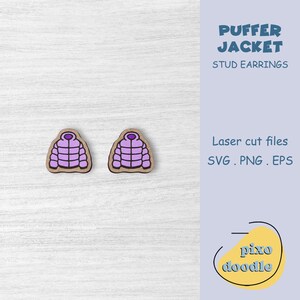 Peut inclure: Deux boucles d'oreilles en forme de doudounes violettes avec un contour marron. Elles sont posées sur une surface en bois blanc. Le texte indique "PUFFER JACKET STUD EARRINGS" et "Laser cut files SVG .PNG .EPS".