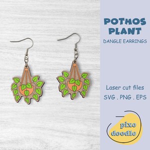 May include: A pair of dangle earrings featuring a laser-cut design of a potted plant with green leaves hanging from a macrame hanger. The earrings are made of wood and have silver hooks. The text "POTHOS PLANT" and "DANGLE EARRINGS" is visible in the image. The text "Laser cut files SVG. PNG. EPS" is also visible in the image.