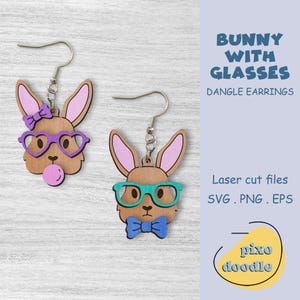 May include: A pair of dangle earrings featuring laser-cut wooden bunny faces. One bunny wears purple heart-shaped glasses and a pink bubble, while the other bunny wears blue and green glasses and a blue bow tie. The earrings are labeled "Bunny with Glasses" and "Laser cut files SVG. PNG. EPS".
