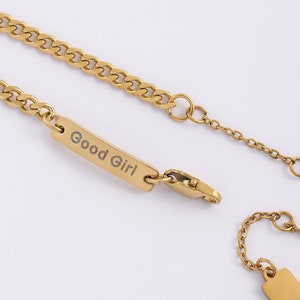 May include: Gold chain necklace with a small rectangular tag that says "Good Girl".