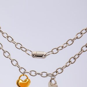 May include: A silver chain necklace with two heart-shaped charms, one gold and one silver. The necklace has a magnetic clasp.