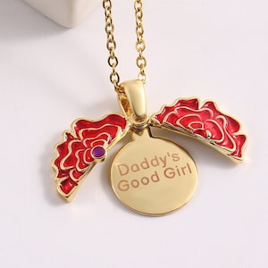 May include: Gold chain necklace with a red rose pendant that opens to reveal a round disc with the inscription "Daddy's Good Girl".
