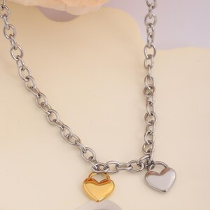 May include: A silver chain necklace with two heart-shaped pendants. One pendant is gold and the other is silver.