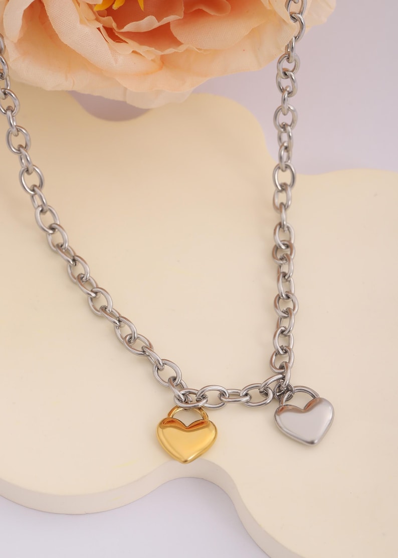 May include: A silver chain necklace with two heart-shaped pendants. One pendant is gold and the other is silver.