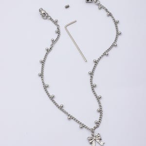May include: Silver-toned necklace with a bow pendant. The necklace features a delicate chain design with small, evenly spaced ball accents. Includes a small screw and a silver-toned hex key. The bow pendant adds a touch of elegance.