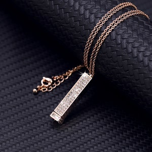 May include: A gold chain necklace with a long, rectangular pendant encrusted with clear sparkling stones.