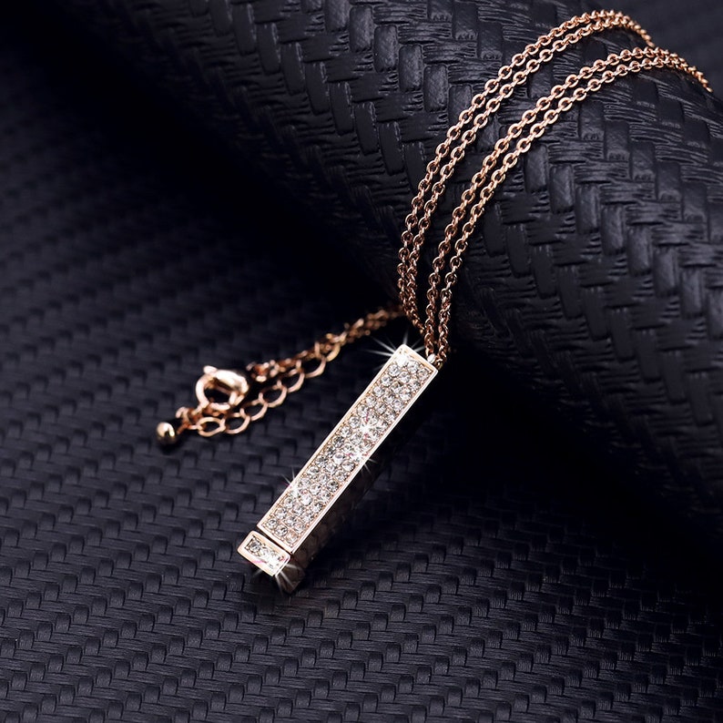 May include: A gold chain necklace with a long, rectangular pendant encrusted with clear sparkling stones.