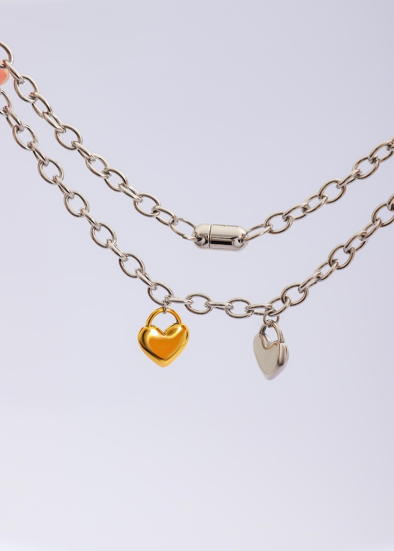 May include: A silver chain necklace with two heart-shaped charms, one gold and one silver. The necklace has a magnetic clasp.
