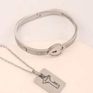 May include: A silver bracelet with a heart-shaped lock and a matching silver necklace with a key pendant. The bracelet has the words "Good Girl" engraved on it and the necklace has the word "Daddy" engraved on it.