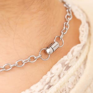 May include: A silver chain necklace with a magnetic clasp. The clasp has the text "Pretty Baby" engraved on it.