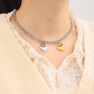 May include: A silver chain necklace with two heart-shaped pendants. One pendant is gold and the other is silver.
