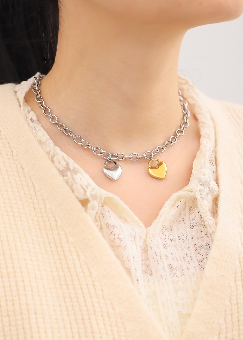 May include: A silver chain necklace with two heart-shaped pendants. One pendant is gold and the other is silver.