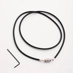 May include: A black rubber necklace with a silver magnetic clasp. The necklace is lying on a white surface.