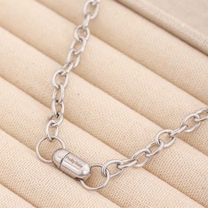 May include: A silver chain necklace with a magnetic clasp. The clasp has the words "Pretty Baby" engraved on it.