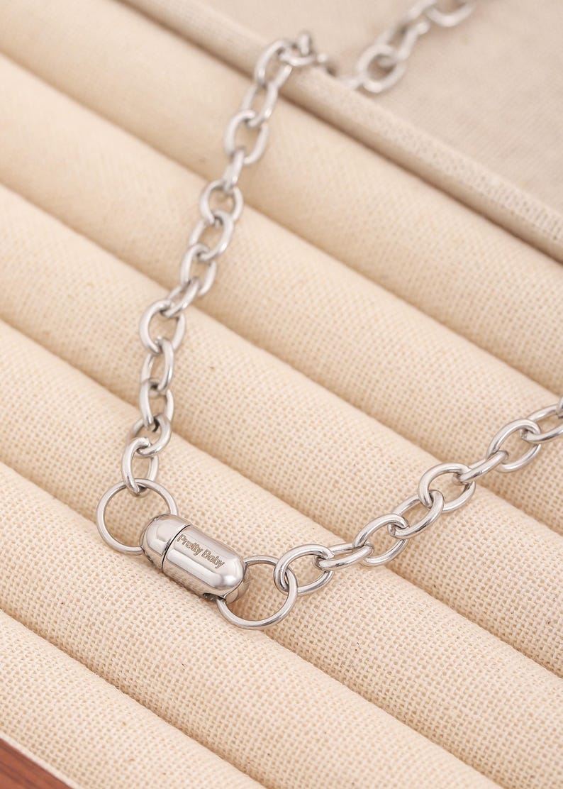 May include: A silver chain necklace with a magnetic clasp. The clasp has the words "Pretty Baby" engraved on it.