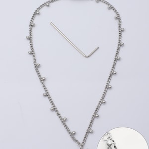 May include: Silver-toned necklace with a bow pendant and small ball accents. Includes a small metal tool and a close-up of the clasp with the text "Custom text". The necklace is on a white background.