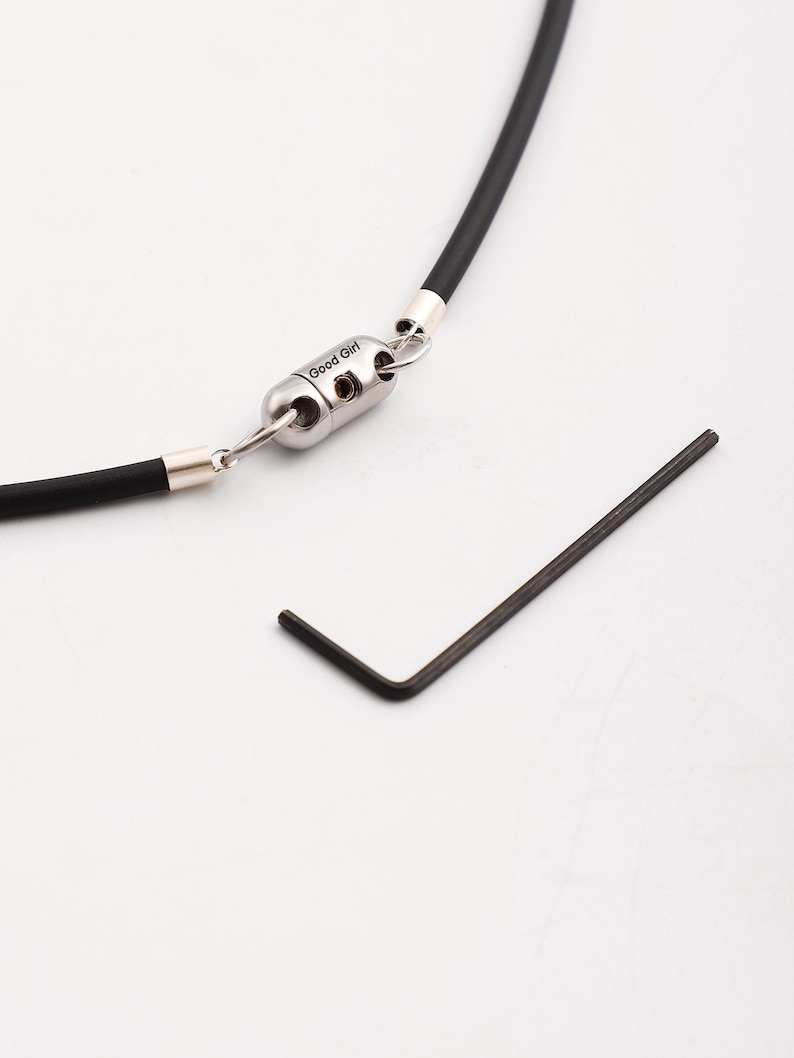May include: A black rubber necklace with a silver clasp that says "Good Girl". A small silver tool is also included.