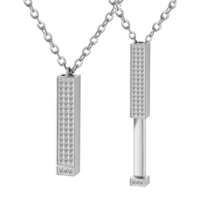 May include: Two silver necklaces with a rectangular pendant covered in small, clear stones. The pendant on the right necklace is open, revealing a silver bar inside.