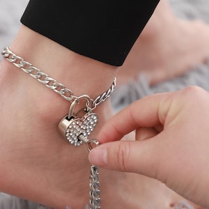 May include: A silver ankle chain with a heart-shaped padlock adorned with rhinestones. The padlock has a key attached to it.