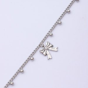 May include: Silver-toned anklet featuring a delicate bow pendant. The chain is adorned with small, round beads. This piece of jewelry is designed to be worn around the ankle.