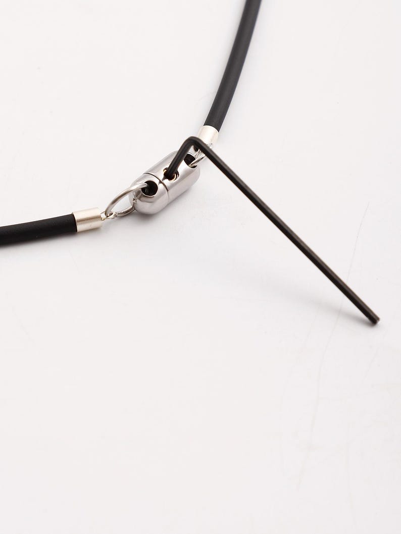 May include: A close-up of a black silicone necklace with a silver clasp and an allen wrench.