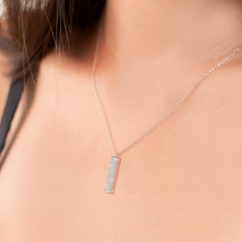 May include: A silver chain necklace with a small, rectangular pendant set with tiny, sparkling stones.