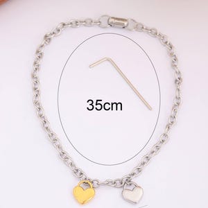 May include: A silver chain bracelet with two heart charms, one gold and one silver. The bracelet is 35 cm long and the charms are 1.4 cm wide.