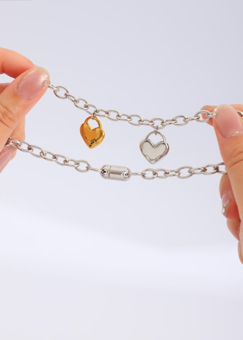 May include: A silver chain necklace with two heart-shaped charms, one gold and one silver. The necklace has a magnetic clasp.
