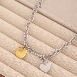 May include: A silver chain bracelet with two heart-shaped charms. One charm is gold and the other is silver.