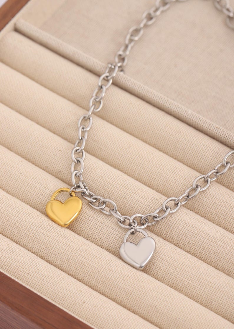 May include: A silver chain bracelet with two heart-shaped charms. One charm is gold and the other is silver.