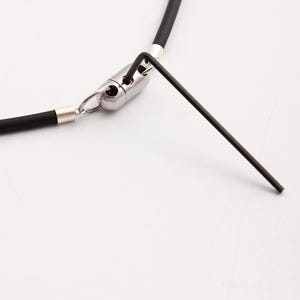 May include: A close-up of a black silicone necklace with a silver clasp and an allen wrench.