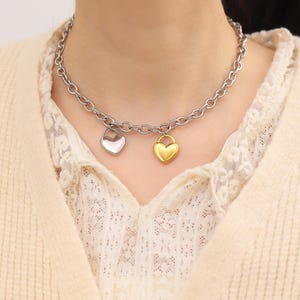 May include: A silver chain necklace with two heart-shaped pendants. One pendant is silver and the other is gold.