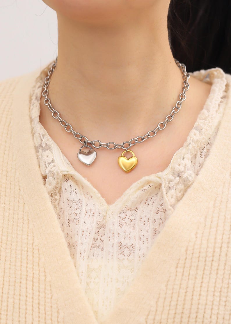 May include: A silver chain necklace with two heart-shaped pendants. One pendant is silver and the other is gold.